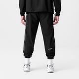 Black ripstop oversized track pants with side stripe, back view on model wearing white socks and sneakers