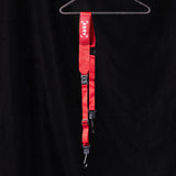 flatlay WN'19 Camera Strap in red, hung on hanger against black background