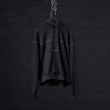 Black contrast thread hoodie displayed on hanger against dark brick wall