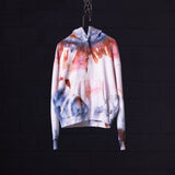 SM'22 Tie Dye Hoodie in white with red and blue tie dye pattern, hanging on chain against dark background