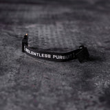 flatlay WN'20 Cobra® Buckle Bracelet with 'Relentless Pursuit' text on grey surface