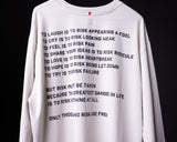 White long-sleeve graphic tee with motivational risk quote text, front view on model