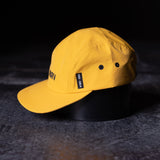flatlay SM'24 5-Panel Run Cap in yellow, angled view on dark surface