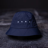 flatlay WN'22 Cinch Bucket Hat in navy blue, front view on dark surface