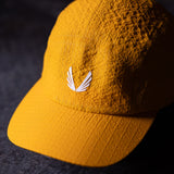 flatlay WN'23 5 Panel Hat in golden yellow, front view on dark surface