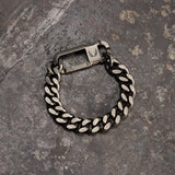 flatlay Carabiner Curb Bracelet in silver-tone metal, overhead view on textured grey surface