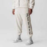 Sherpa Recovery Sweats in ivory cream with black text detail, worn by model, full-length front view