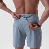 Revolutional® Board Short in Light Sky, worn by model, front view with hands adjusting waistband
