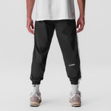 Black ripstop oversized track pant worn by model, back view with white socks and sneakers