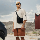 Black water bottle holster bag worn as crossbody on model in white tee and brown shorts